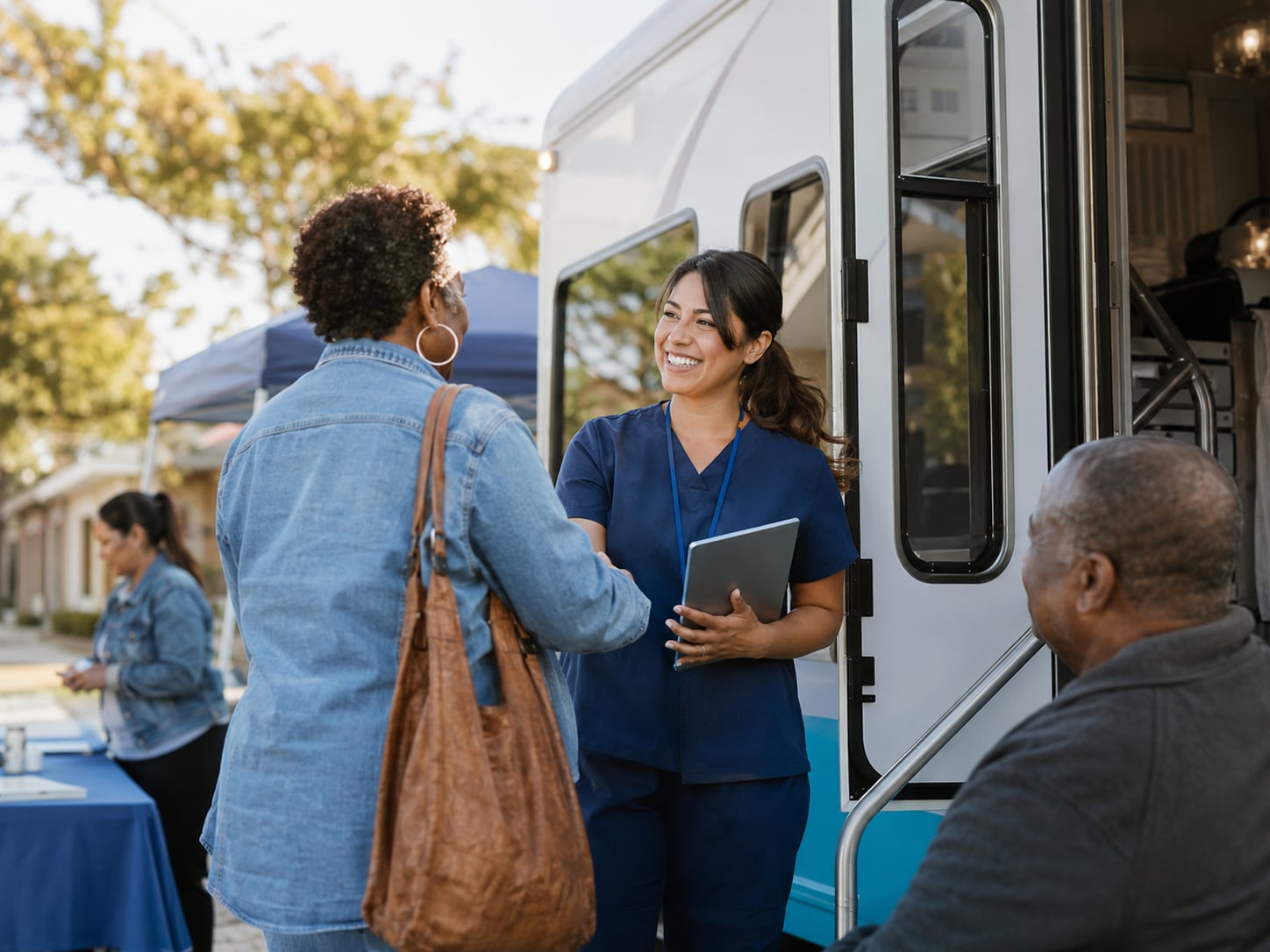 A nurse shakes hands with an older woman outside a mobile clinic van, while an older man sits nearby.